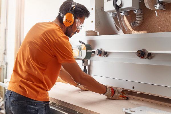 Firefly cabinet factory, with close up shot working on surfacing machine wearing orange